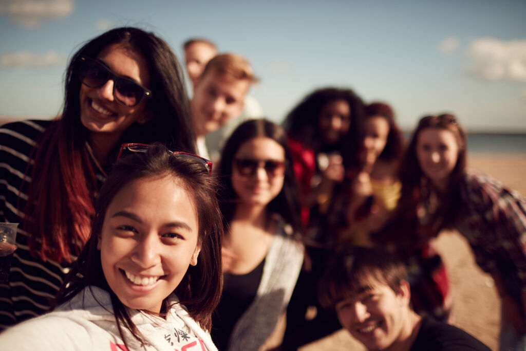 A group of students, smiling for a selfie on the beach