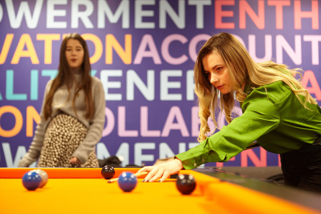 Two students playing pool, the pool table is yellow which is unusual as they are generally green