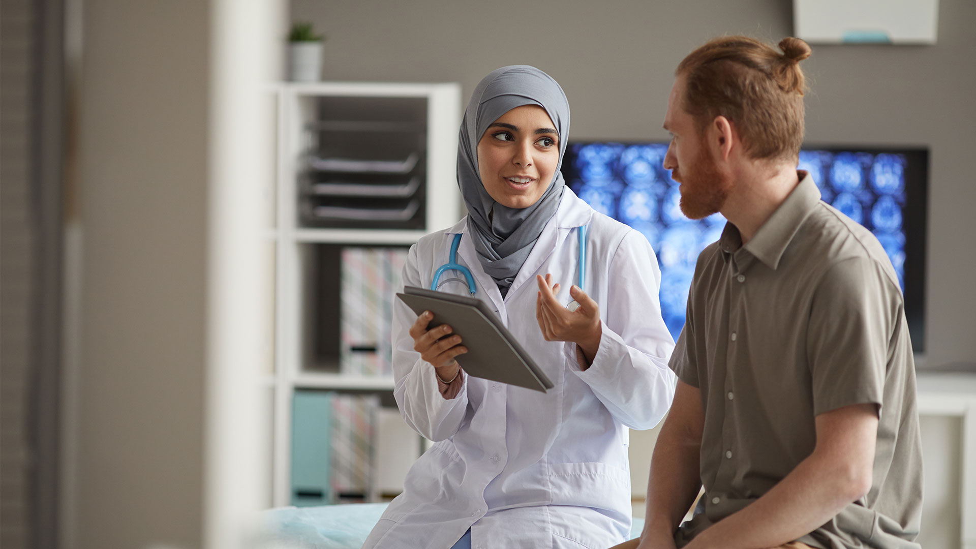 A female health professional holds a tablet device whilst talking to a male patient