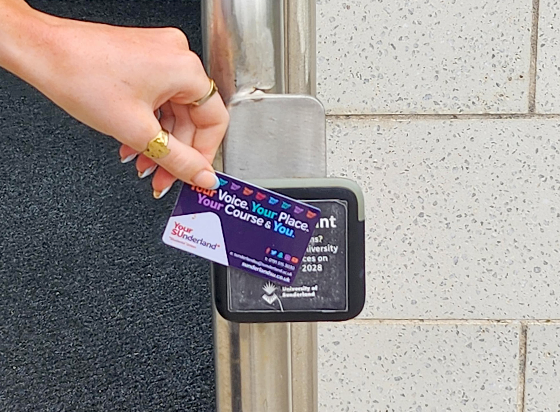 A hand holding a campus card holds the card against the reader in order to gain access to a building