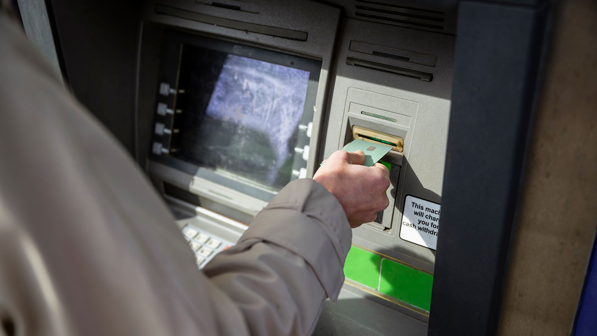 A hand inserts a bank card into a cash machine.