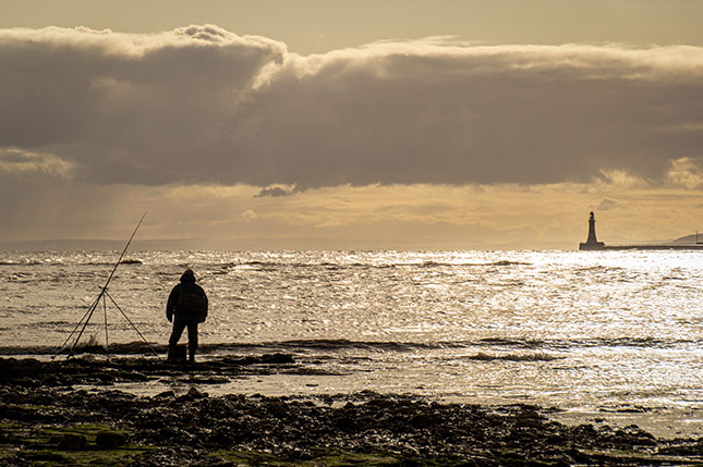 The silhouette of a human man fishing in the North Sea from Roker