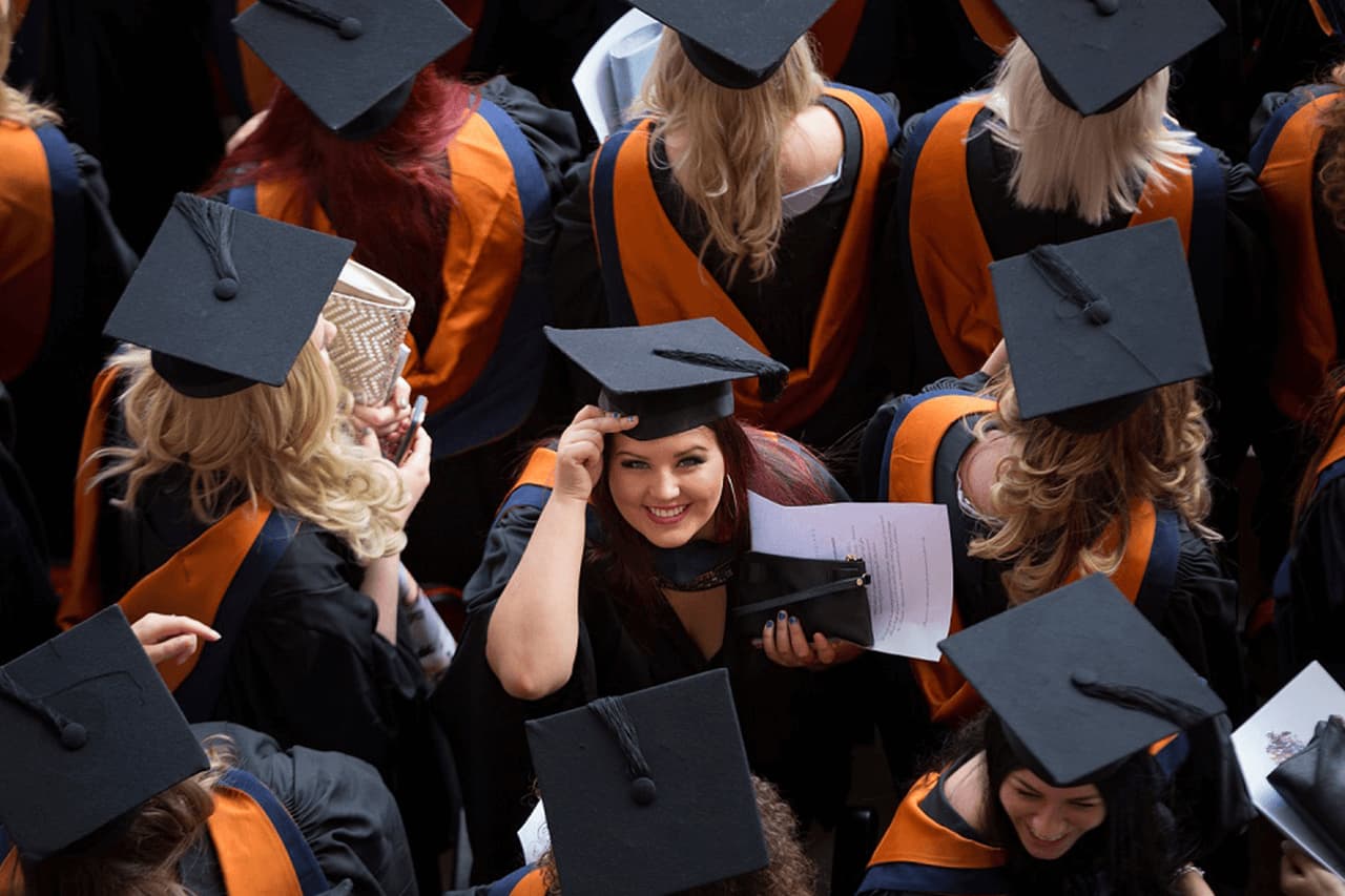 A birds eye view of students dressed in graduation ceremonial gowns and mortar boards. One student in the centre is smiling up at the camera.