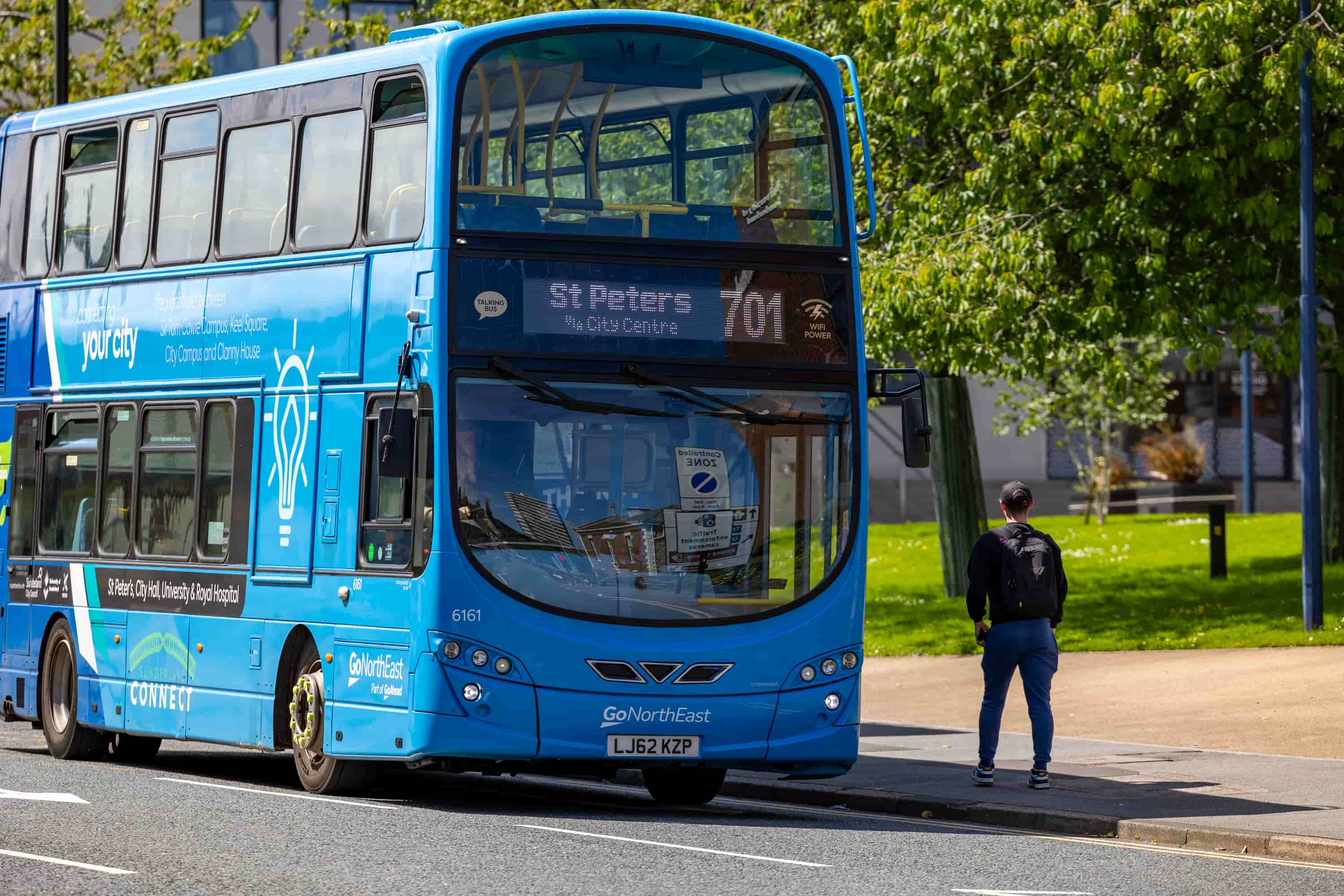 The blue campus bus parked up at city campus with a student waiting for it